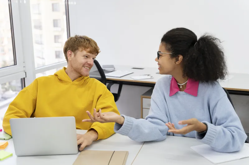 Zwei Kolleginnen und Kollegen besprechen ihre Arbeit am gemeinsamen Schreibtisch